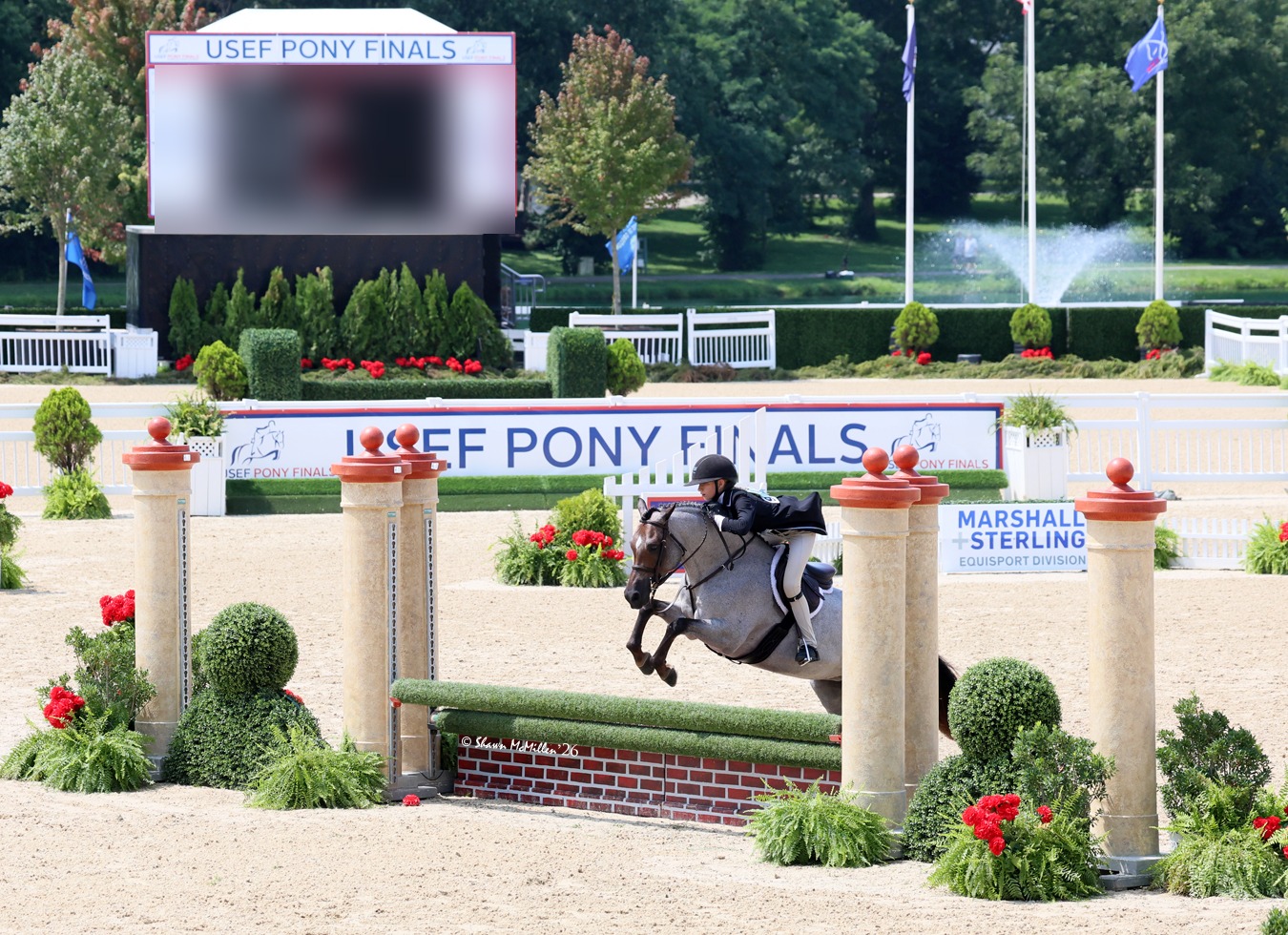 Rider jumping in the USEF Pony Finals ring beneath the scoreboard